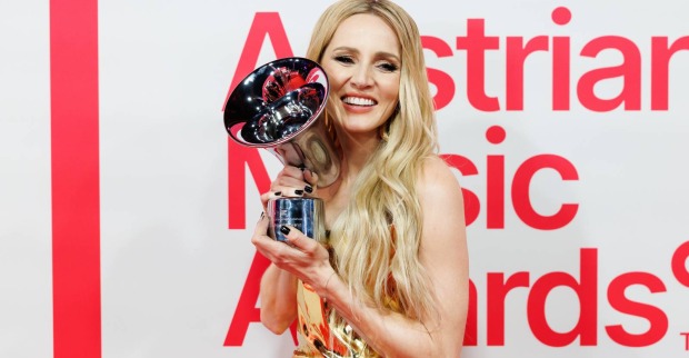 Melissa Naschenweng auf dem Roten Teppich des Amadeus Austrian Music Awards, die eine der Auszeichnungen mit zwei Händen neben ihr Gesicht hält