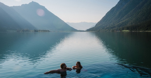 Pärchen beim Schwimmen in einem See bei Sonnenaufgang | Credit: Tirol Werbung/Dominic Zimmermann