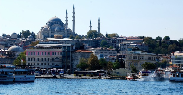 Panorama von Istanbul mit der Süleymaniye-Moschee im Hintergrund, davor der Bosporus mit mehreren Booten und Fähren bei sonnigem Wetter.