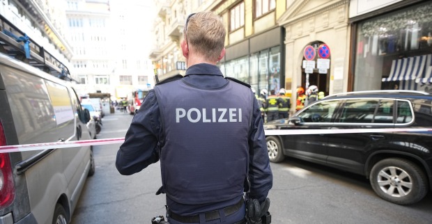 Polizist mit Schutzweste sichert Brandort in der Wiener Innenstadt ab, im Hintergrund Feuerwehrleute vor einem Gebäude in der Spiegelgasse.