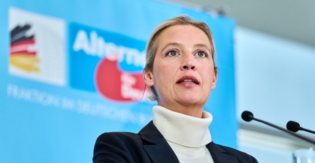 Alice Weidel, AfD-Bundesvorsitzende, spricht auf einer Pressekonferenz vor einem blauen Hintergrund mit AfD-Logo und Mikrofonen.