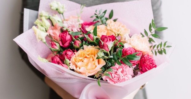 Frau in grauem Pullover hält bunten Blumenstrauß in rosa Verpackungspapier