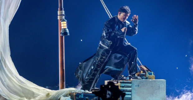 JJ beim ESC 2025-Halbfinale auf einer symbolischen Segelboot-Bühne in Schwarz-Weiß-Optik, gekleidet in langen Mantel und umgeben von Nebel.