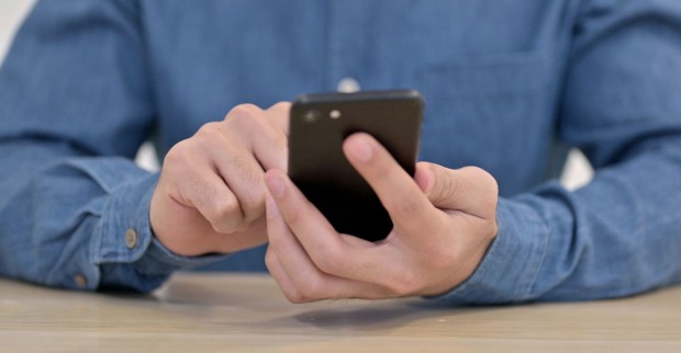 Nahaufnahme einer Person in Jeanshemd, die mit einem Smartphone in der Hand auf den Bildschirm tippt – kein Empfang erkennbar.