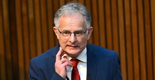 Markus Marterbauer, SPÖ-Finanzminister, spricht im Nationalrat. Er trägt einen blauen Anzug, eine rote Krawatte und eine Brille. Im Hintergrund sind Holzlamellen sichtbar.
