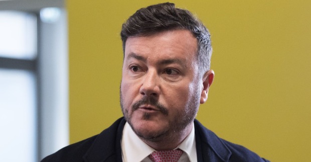 René Benko blickt ernst zur Seite, im Hintergrund eine gelbe Wand.