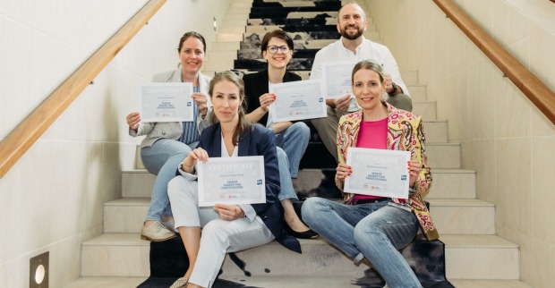Absolventen des "Senior Marketing Professional"-Programms sitzen mit ihren Urkunden auf einer Stiege