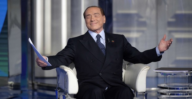 Silvio Berlusconi sitzt im TV-Studio und breitet gönnerhaft die Arme aus