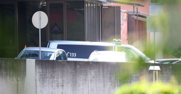 Polizeifahrzeuge stehen vor einem Wohngebäude hinter einer Mauer, Nummer 133 sichtbar, Szene abgeschirmt und teilweise von Grün verdeckt.