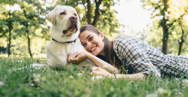 Frau liegt neben einem Hund im Gras