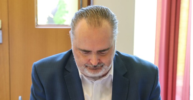 Hans Peter Doskozil blickt nach unten, trägt ein dunkles Sakko und ein weißes Hemd, im Hintergrund ein Fenster mit rotem Vorhang.
