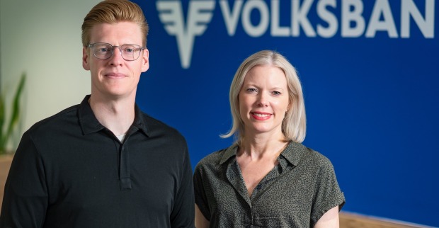 Mann mit Brille und schwarzem Shirt und Frau mit Bluse im Printlook vor einer blauen Wand
