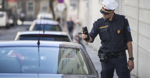 Straßenaufsichtsbeamter in Uniform scannt den Parkschein eines parkenden Auto in Wien mit einem mobilen Kontrollgerät.