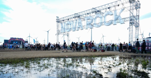 Nova Rock-Festivalgelände mit kleinem Gewässer und Eingangspforte mit Aufschrift "Nova Rock" und Menschen