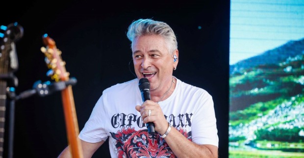 Didi Ganshofer, Sänger der Paldauer, mit Mikrofon auf der Bühne, lächelnd in einem weißen T-Shirt mit Tigerprint – Aufnahme vor seinem Schlaganfall.