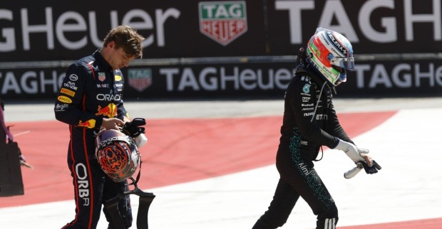 Red-Bull-Fahrer Verstappen hält seinen Helm und blickt frustriert zu Boden, während Mercedes-Pilot Antonelli mit Helm und Handschuhen davonläuft – Szene nach einem Unfall auf einer Formel-1-Strecke.