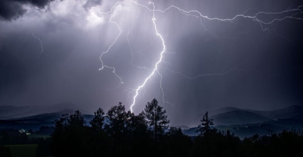 Ein Gewitter mit Blitzen über einem Wald.