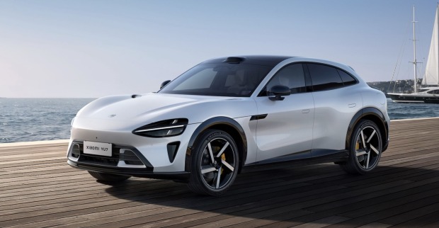 Der weiße Xiaomi YU7 Elektro-SUV steht auf einem Holzsteg vor dem Meer, im Hintergrund ein Segelboot – sportlich-elegantes Fahrzeug mit aerodynamischer Linienführung.