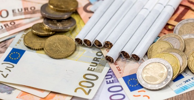 Zigaretten liegen auf Euronoten, daneben liegen Euromünzen