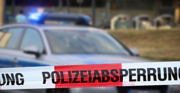Polizeiwagen an einem Tatort, davor ist ein Polizeiabsperrband befestigt