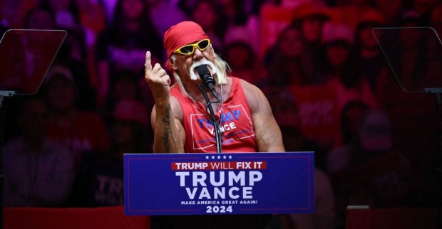 Hulk Hogan steht mit rotem Bandana und Sonnenbrille hinter einem Rednerpult mit der Aufschrift „Trump – Vance 2024“ und spricht bei einer Wahlkampfveranstaltung.