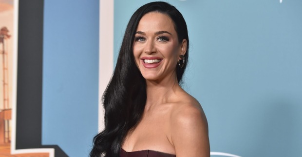 Katy Perry mit offenen, schwarzen Haaren vor blauem Hintergrund