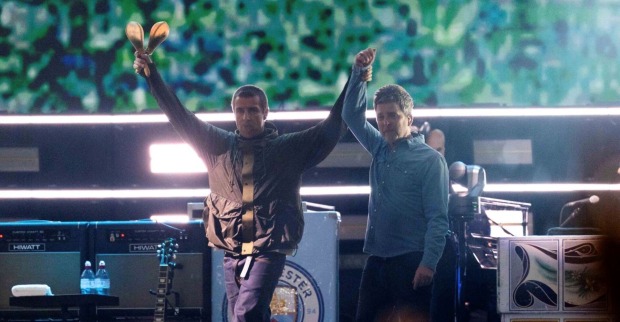 Liam hält Noel Gallaghers Hand, im Hintergrund sieht man ein Wappen des Fußballclubs Manchester City