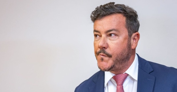 René Benko, im blauen Anzug mit roter Krawatte, verzieht das Gesicht und schaut zur Seite