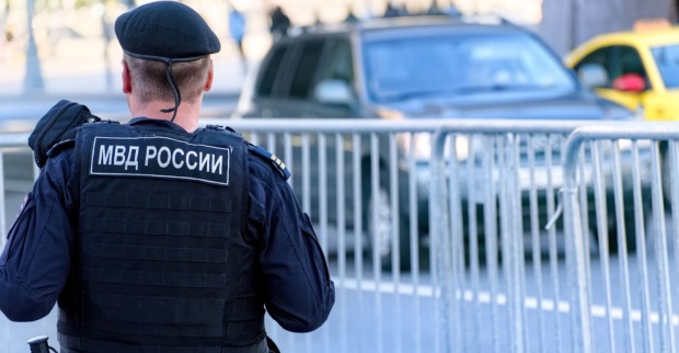 Russischer Polizist der Nationalgarde in kugelsicherer Weste patrouilliert durch die Straßen der Stadt, vor ihm ist ein Zaun, dahinter ein Auto