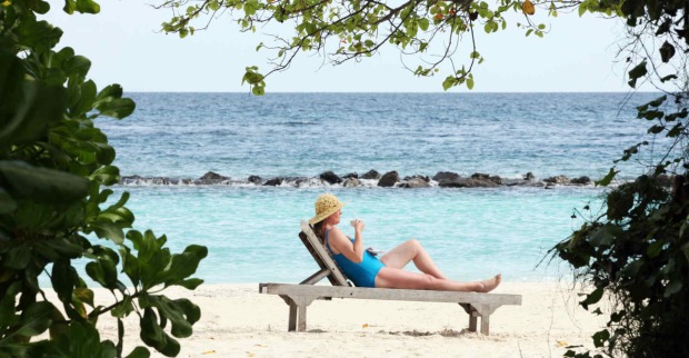 Frau im Badeanzug und mit Sonnenhut liegt auf einer Liege am Strand