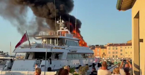 Luxusyacht „Sea Lady II“ brennt im Hafen von Saint-Tropez, schwarze Rauchwolken und hohe Flammen steigen auf, Passanten beobachten und fotografieren das Feuer.