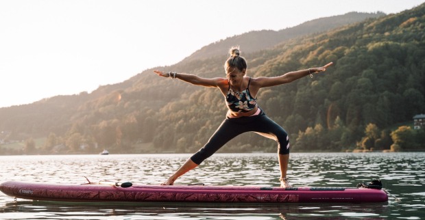 Eine Frau macht Yoga auf einem SUP auf dem Wasser.
