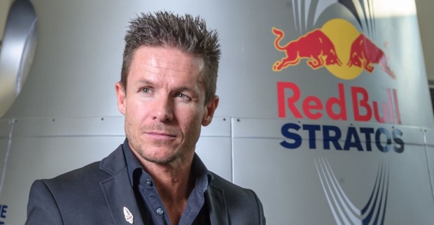 Felix Baumgartner steht in einem dunklen Anzug vor der Red Bull Stratos-Kapsel mit dem Red Bull Logo im Hintergrund.