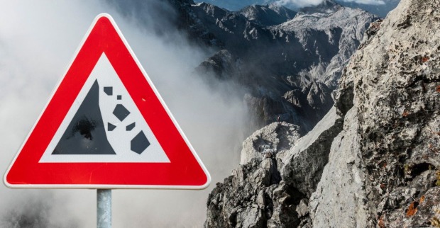 Fotoaufnahme der bayrischen Alpen im nebel, neben einem Warnschild vor Felsstürzen