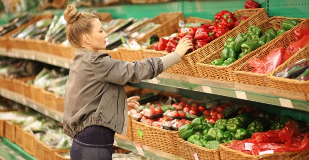Frau mit Zopf greift im Supermarkt nach rotem Paprika