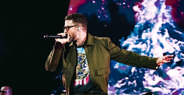 Justin Timberlake singt auf der Bühne, trägt ein gestreiftes Jackett und ein T-Shirt mit Grafikdruck, im Hintergrund eine farbige Lichtinstallation.