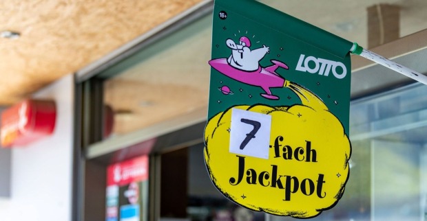 Grünes Lotto-Plakat mit gelber Wolke und der Aufschrift „7-fach Jackpot“ vor einer Trafik in Österreich.