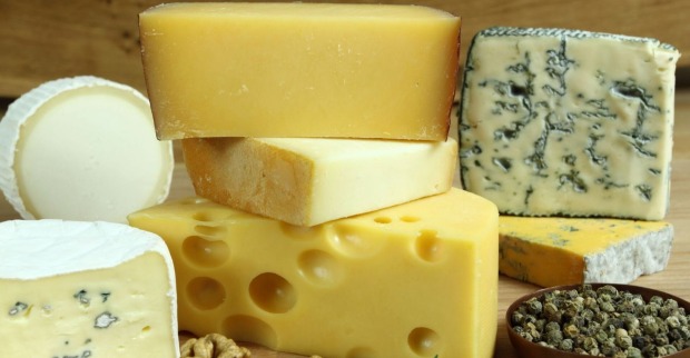 Verschiedene Käsesorten, darunter Camembert, Blauschimmelkäse, Emmentaler und Hartkäse auf einem Holzbrett, daneben Pfefferkörner.