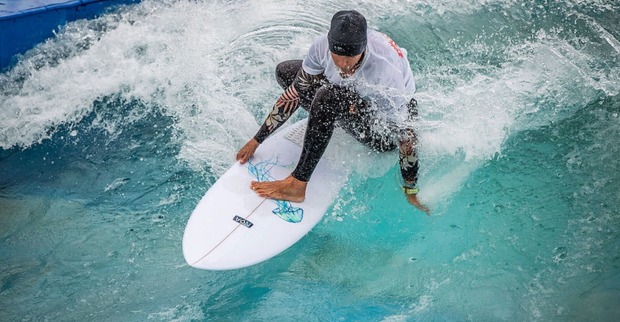 Surfer im schwarzen Neoprenanzug, weißem Shirt und schwarzer Haube reitet die Welle