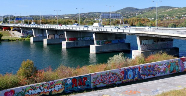 Blick auf eine Brücke über die Neue Donau in Wien, mit bunten Graffiti an den Brückenpfeilern und Mauern im Vordergrund. Im Wasser unterhalb der Brücke wurde eine Leiche gefunden.