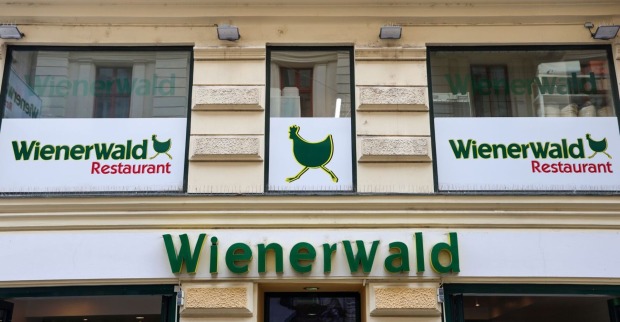 Logo des Wienerwald-Restaurants und Schild mit dem Symbol des laufenden Huhns an einer Gebäudefassade