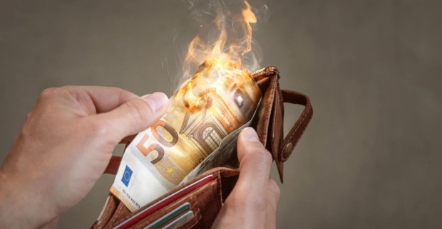 Eine Hand hält eine Geldbörse, aus der ein brennender 50-Euro-Schein ragt – Symbol für die steigende Inflation und Kaufkraftverluste.
