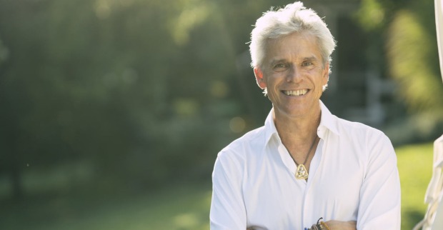 Thomas Brezina lächelt im weißen Hemd in die Kamera, Hintergrund Garten, Fokus auf seine Person.