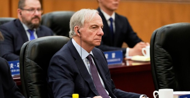 Ray Dalio sitzt im Anzug mit Kopfhörern bei einer Konferenz am Tisch, konzentrierter Gesichtsausdruck, weitere Teilnehmer im Hintergrund.