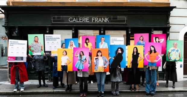 Gruppenbild vor Galerie mit Frauen, die große Porträts von sich hochhalten