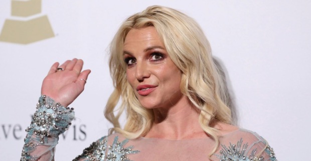 Britney Spears winkt bei einem Auftritt in einem glitzernden, hellblauen Kleid mit silbernen Verzierungen.