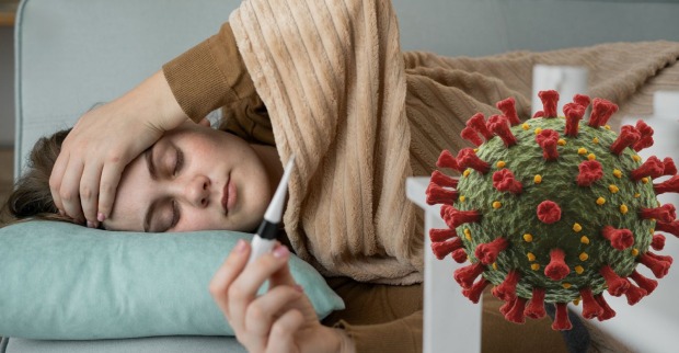 Frau liegt krank mit Thermometer im Bett, Symbolbild für Infektion mit der Corona-Variante XFG „Stratus“.