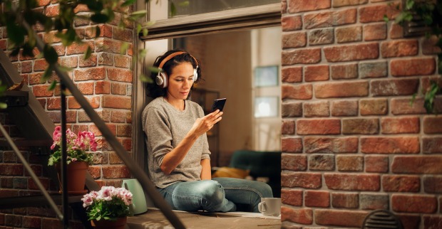 Frau sitzt am Fenster und hört einen Podcast | Credit: iStock.com/gorodenkoff