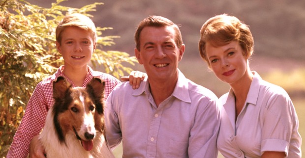 Die Martin-Familie aus der Fernsehserie „Lassie“ sitzt gemeinsam mit dem Collie Lassie im Freien und lächelt in die Kamera.