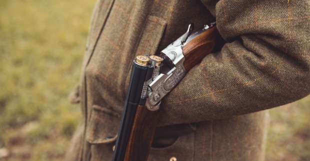 Jäger auf einem Feld stehend mit einer Schrotflinte in seinem linken Arm